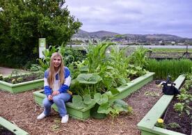 catherine webb sitting in front of vegetables in a garden